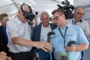 メカトロニクスの研修生ニコライ・モースナーが、バーデンヴュルテンベルク州のミニスター・プレジデントのウィンフライド・クレチェトマンとデジタリゼーション・ミニスターのトーマス・ストローブルに、印刷機のバーチャルワールドを紹介。